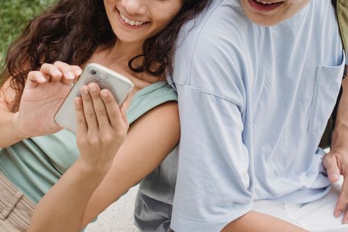 Free From above of crop anonymous happy couple sharing mobile phone while resting on city bench in summer Stock Photo