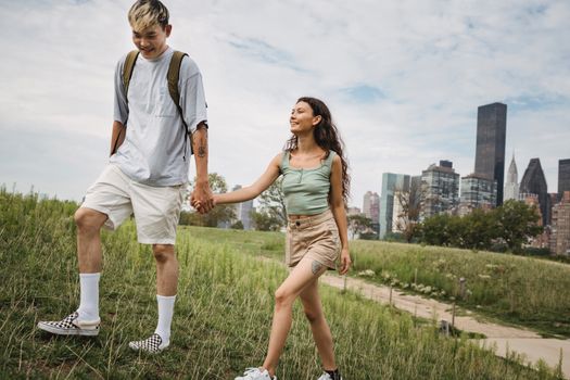 一对多种族夫妇手牵着手，高兴地漫步在镇上多云的绿色山坡上