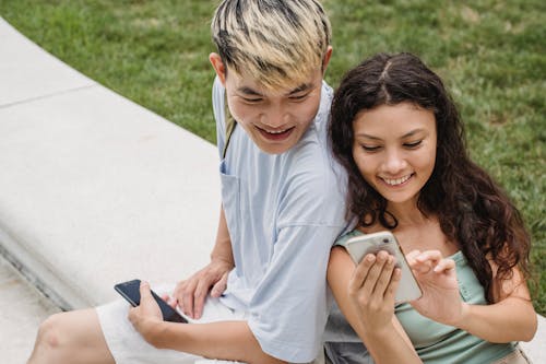 Charming ethnic woman showing smartphone to Asian partner on bench