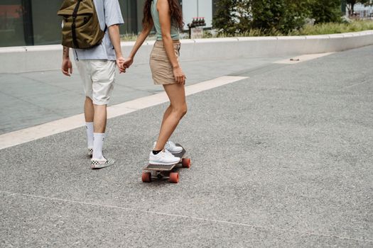 一对夫妇在夏季的城市街道上牵着手玩滑板，享受漫步的乐趣