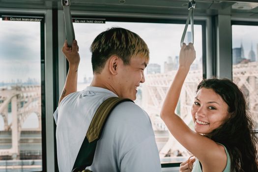 Young happy multiethnic tourists laughing in cable car with raised arms while traveling together