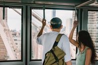 Back view faceless couple in casual clothes riding funicular cabin and grabbing hangers while looking away on urban city views