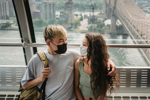 一对恩爱的情侣戴着口罩，在俯瞰城市景观的缆车里拥抱