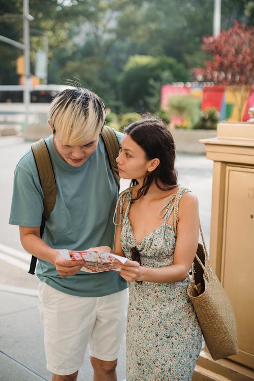 Young lost couple standing on city street and looking at map while travelling together in city