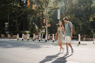 Full body of happy young girlfriend carrying bag while walking on asphalt crosswalk with boyfriend