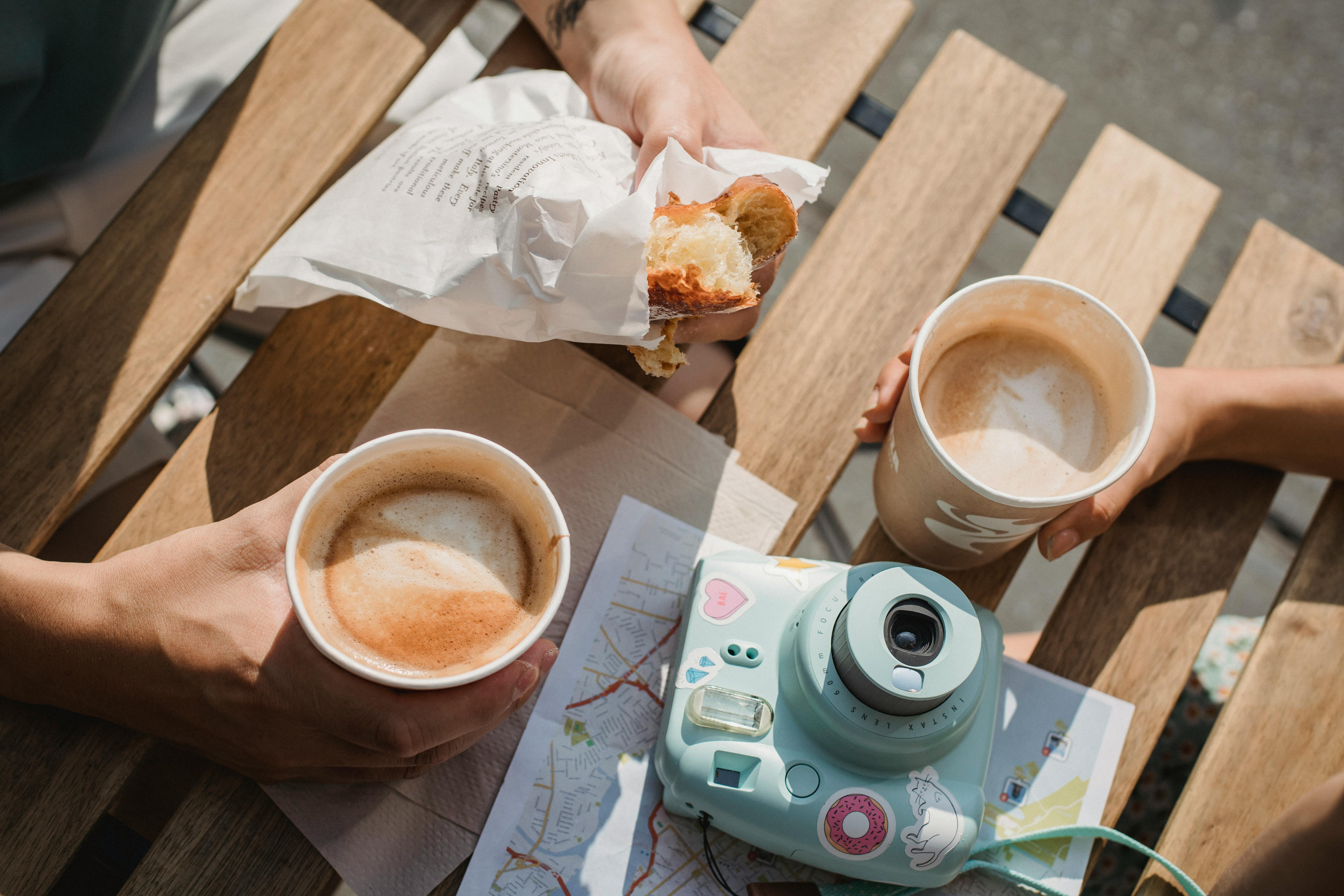 unrecognizable couple with takeaway coffee and pastry at cafe table