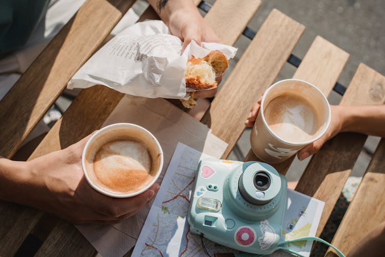 Unrecognizable Couple With Takeaway Coffee And Pastry At Cafe Table