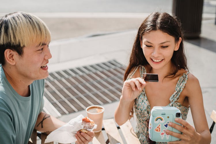 Happy Diverse Couple Watching Instant Photo In Street Cafe