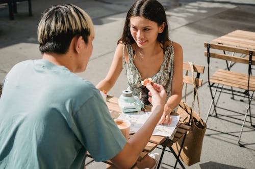 Smiling ethnic woman talking to unrecognizable boyfriend in street cafeteria