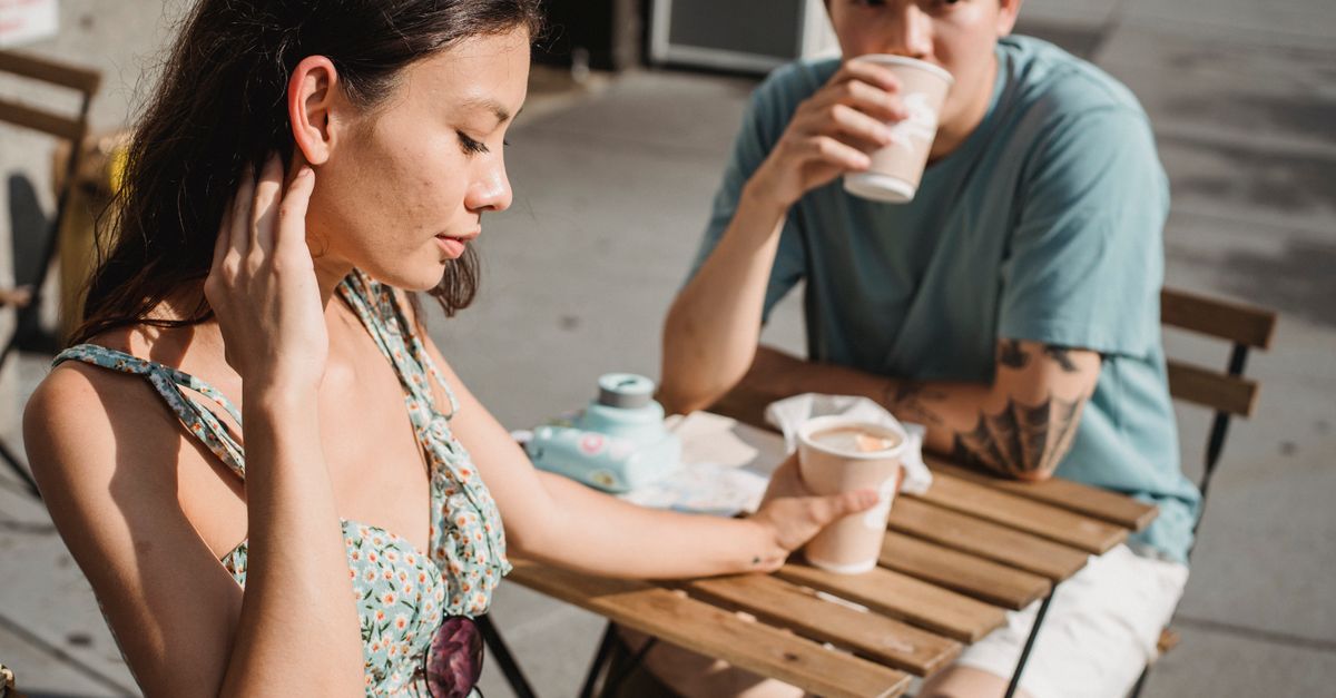 Young tender dreamy girlfriend and Asian pensive boyfriend with cup of hot coffee on sunny street