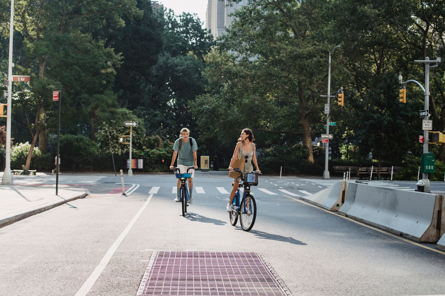 Couple riding bicycles on asphalt roadway in city against green trees in sunny day