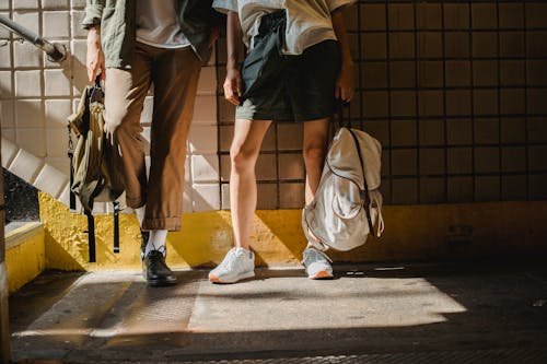 Lower body parts of crop anonymous stylish couple leaning on tiled wall in pedestrian passage