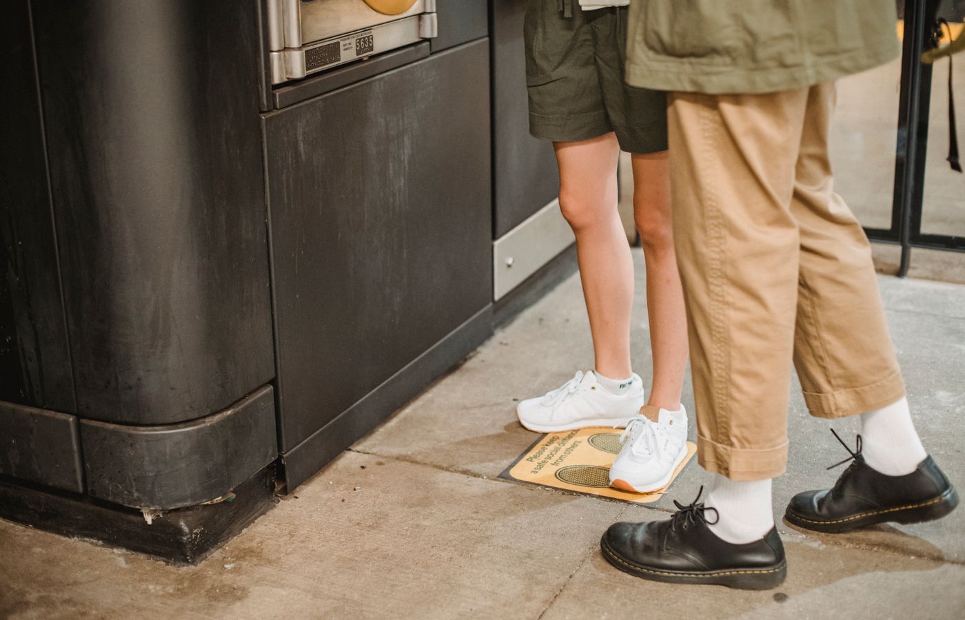 Casual couple standing by a vending machine in a trendy urban setting, focusing on footwear.