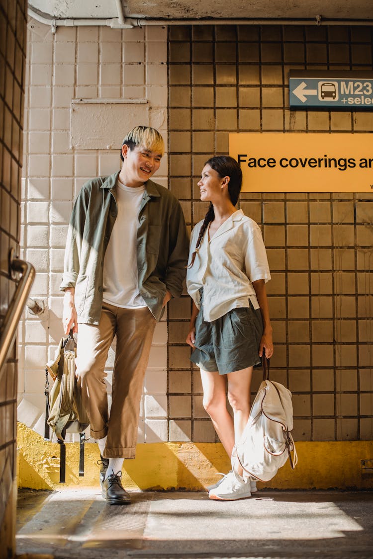 Cheerful Asian Couple Standing Near Tiled Wall And Talking