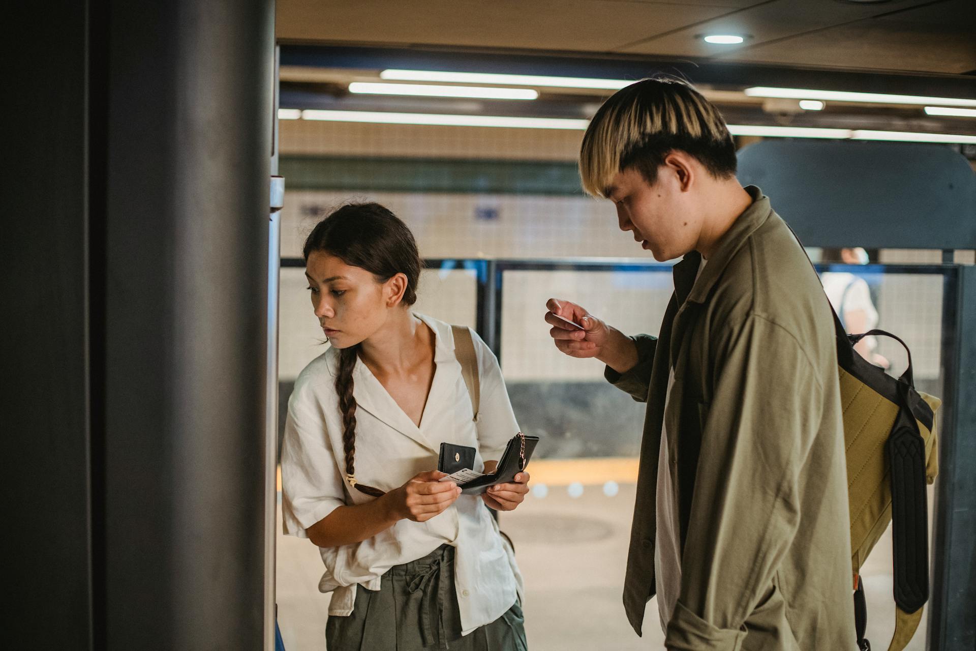 Concentrated Asian couple in casual clothes with wallet and credit cards in hands standing in underground passage