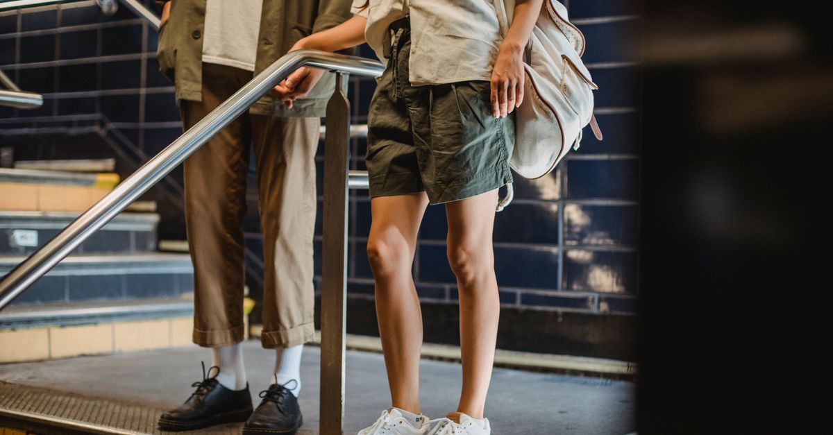 Crop anonymous couple in casual outfits standing near stairs railing in modern underground