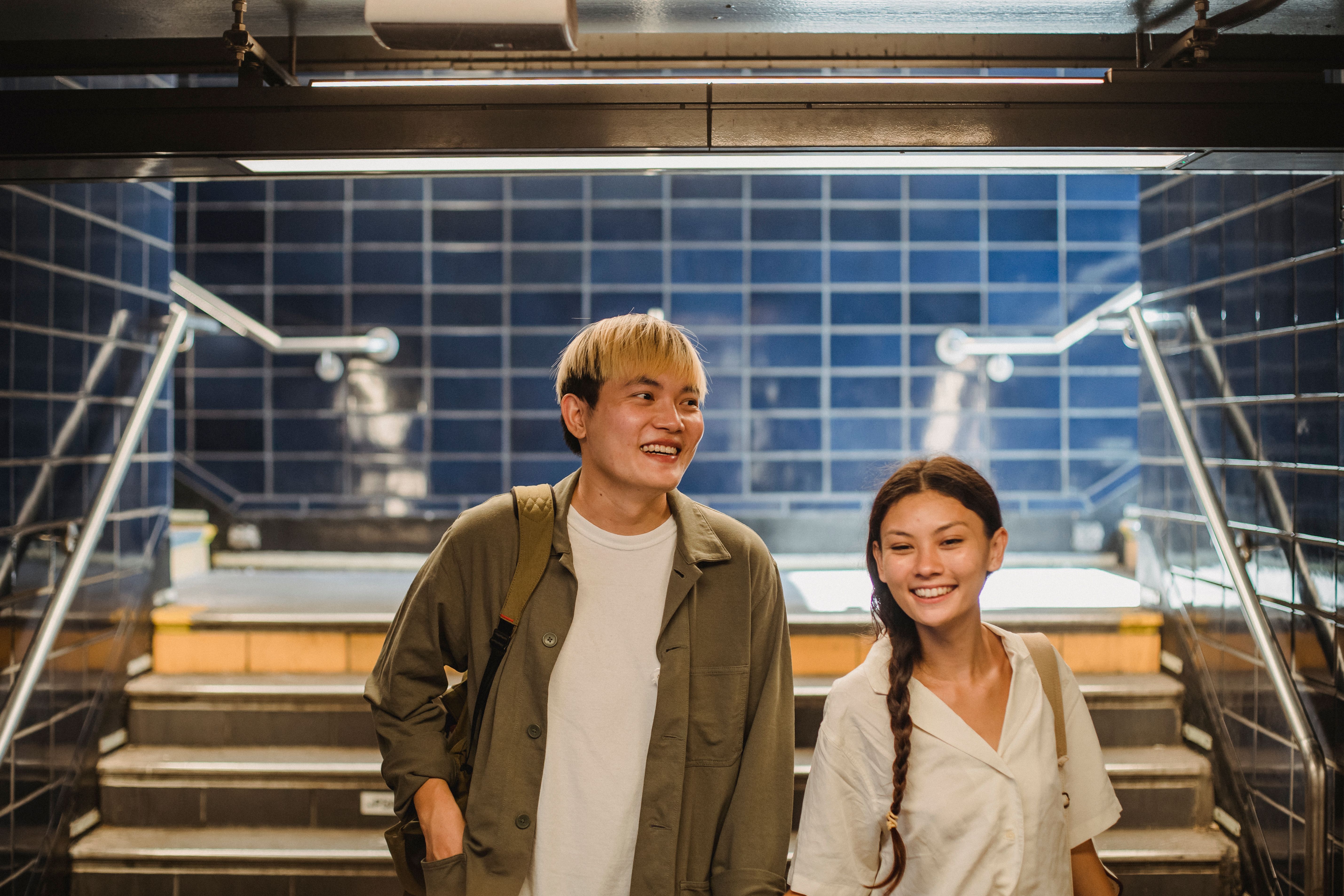Free Cheerful young Asian couple in casual outfits walking downstairs in underground hallway and smiling Stock Photo