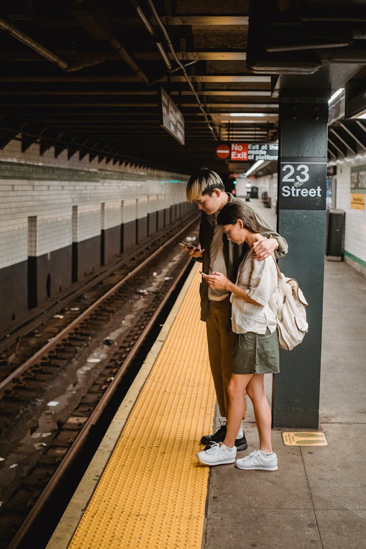 Concentrated Asian Couple Using Mobile Phones In Metro Station