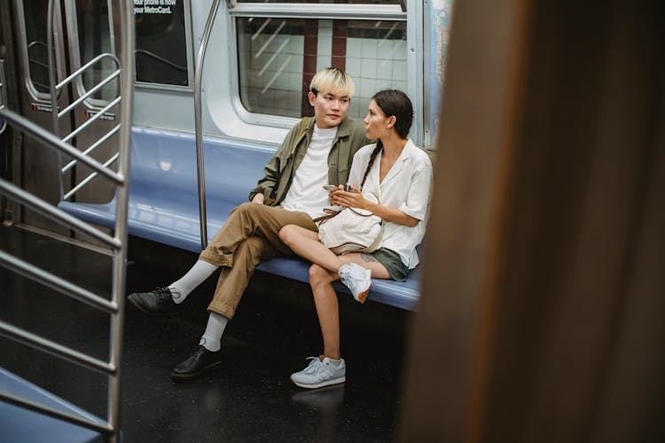 Trendy Young Asian Couple Looking At Each Other While Riding Train