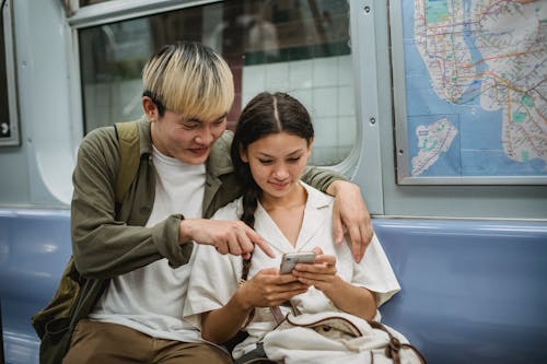 Pasangan Etnis Muda Yang Positif Merangkul Dan Menggunakan Smartphone Di Kereta