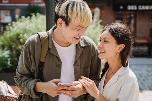 Positive young multiethnic couple smiling and looking at each other on street