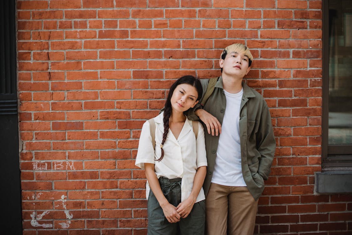 Free Young stylish multiracial couple leaning on brick wall while chilling on street on sunny day Stock Photo