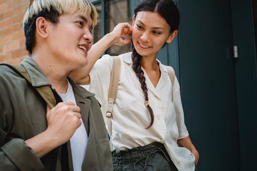 Crop happy Asian couple in stylish outfits standing near building entrance and having conversation