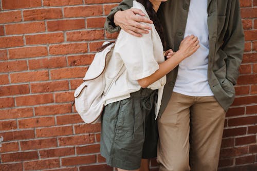 Free Crop unrecognizable romantic couple wearing trendy summer clothes embracing each other against masonry wall Stock Photo