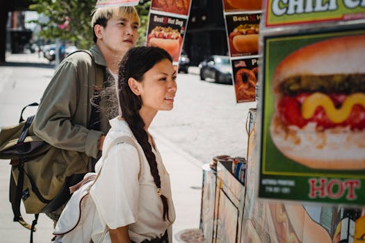 A young couple looks at a street food stand on a sunny day in an urban setting, enjoying a carefree moment together.