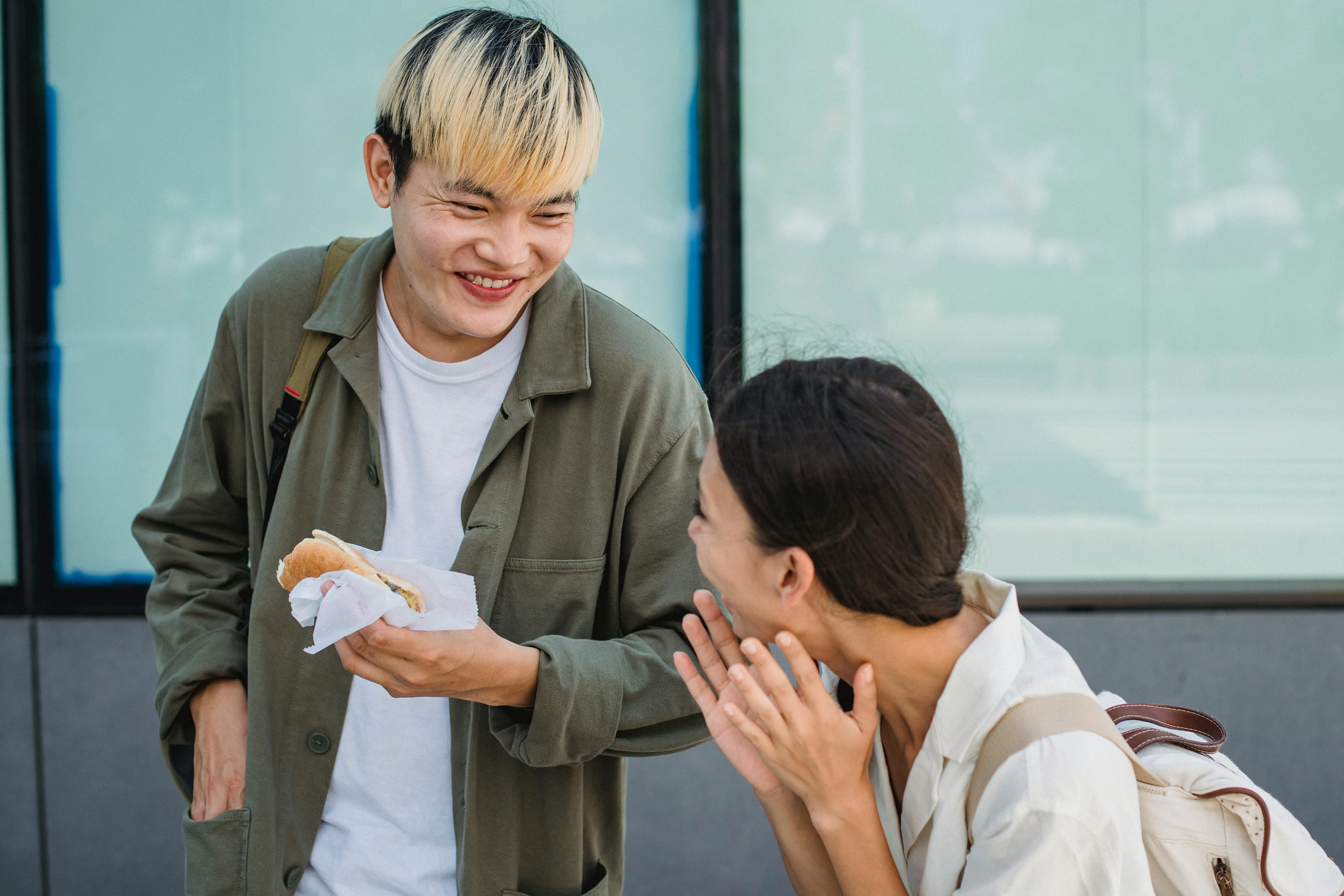joyful asian couple enjoying hot dog on street