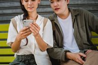 一对亚洲夫妇坐在户外，正一起浏览智能手机，享受着这个积极的时刻