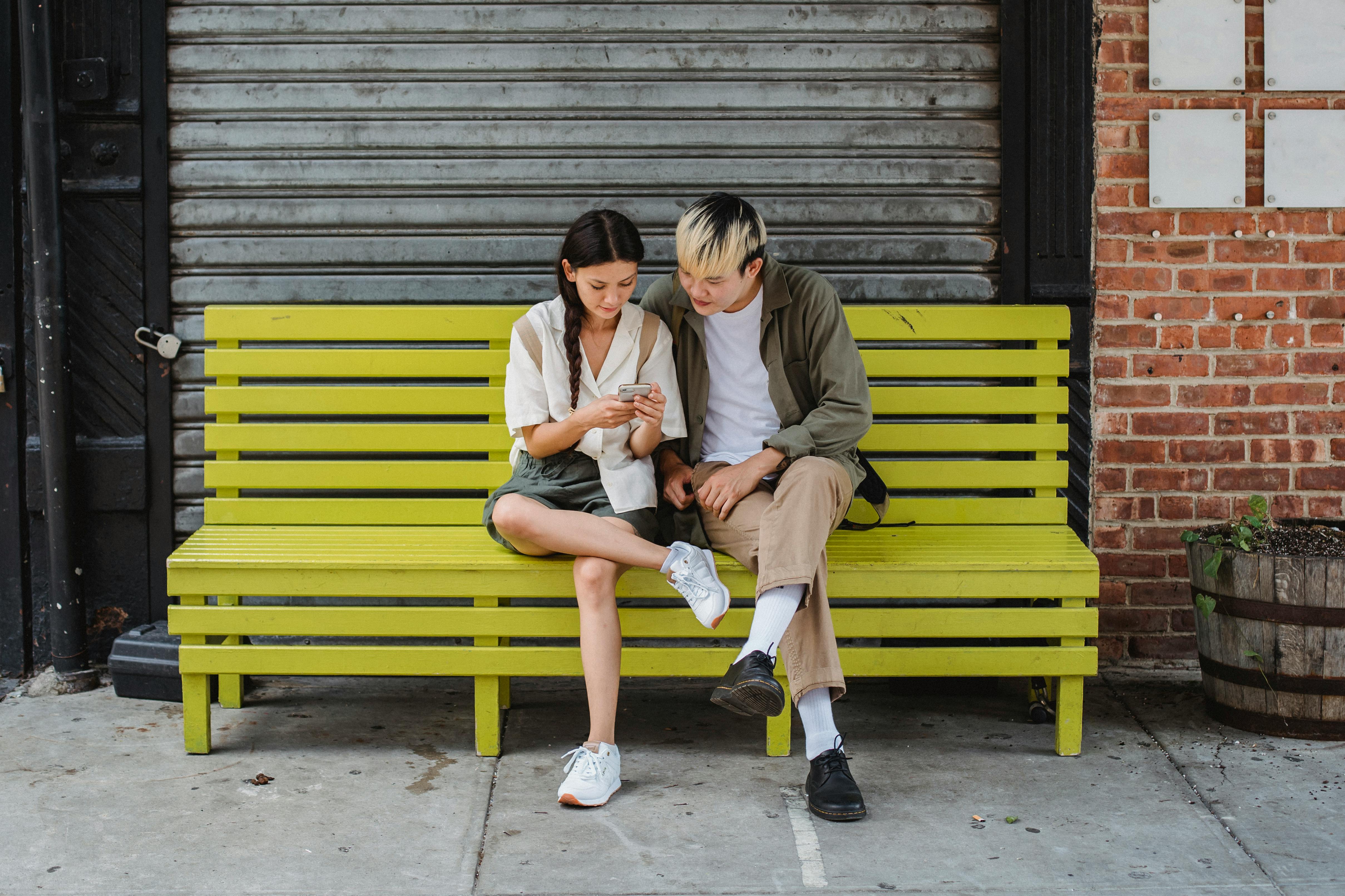 concentrated friends sitting on bench and using smartphone