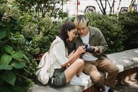 Asian couple using modern photo camera in lush park