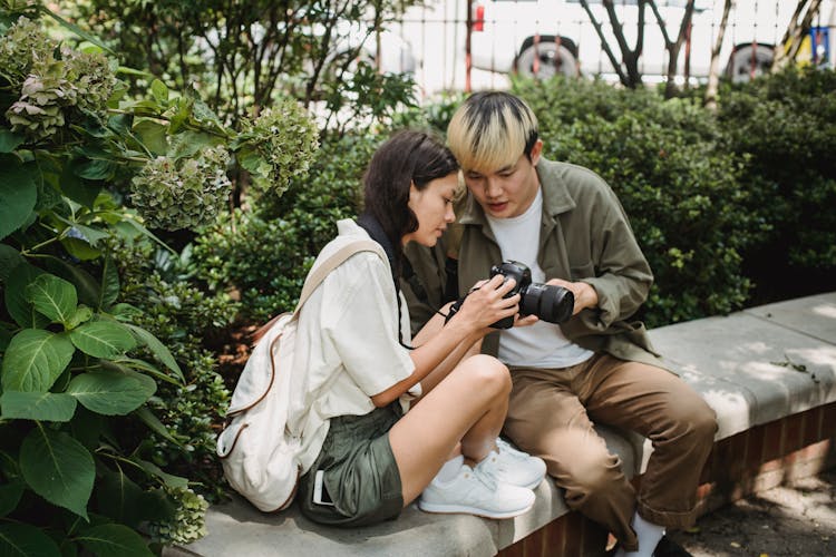 Asian Couple Using Modern Photo Camera In Lush Park