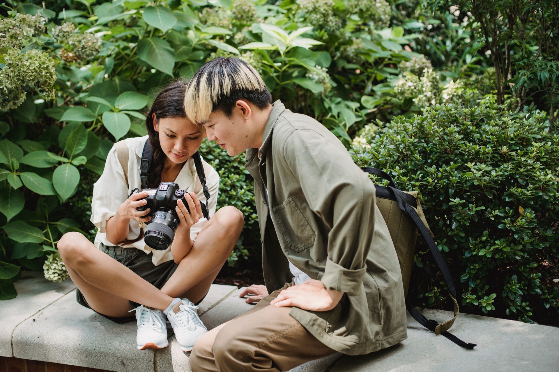 A young couple examining photos on a digital camera amidst lush greenery.