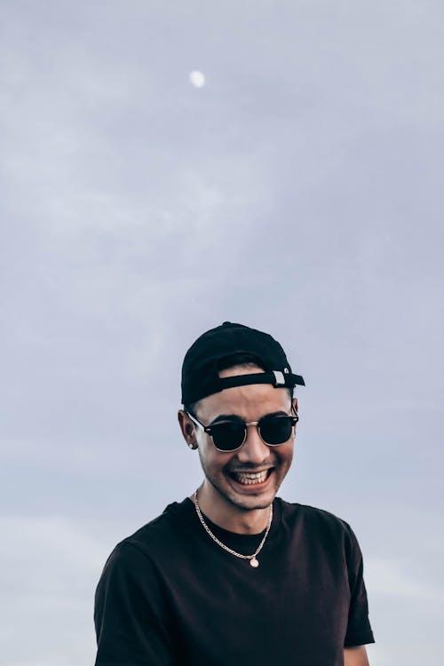 Joyful man in sunglasses standing against gray sky