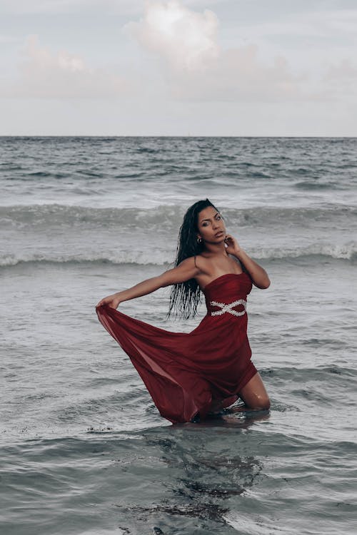 Graceful ethnic woman in wet maxi dress standing in seawater