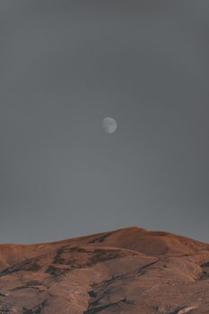A captivating landscape of a full moon shining over rugged mountain peaks under a clear night sky.