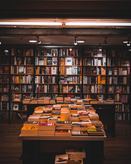 Free Warmly lit bookstore with bookshelves and stacks of books, perfect for reading enthusiasts. Stock Photo
