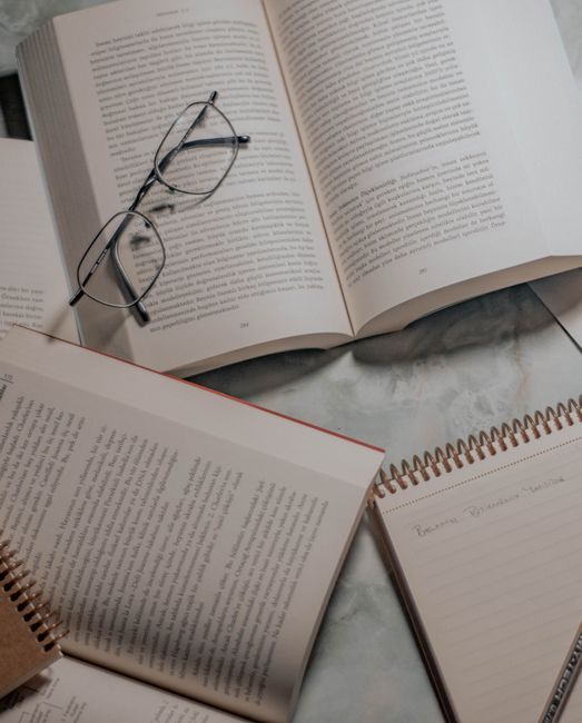 Open books and glasses on a marble table, with notepad for study or research context. Open books and glasses on a marble table, with notepad for study or research context.