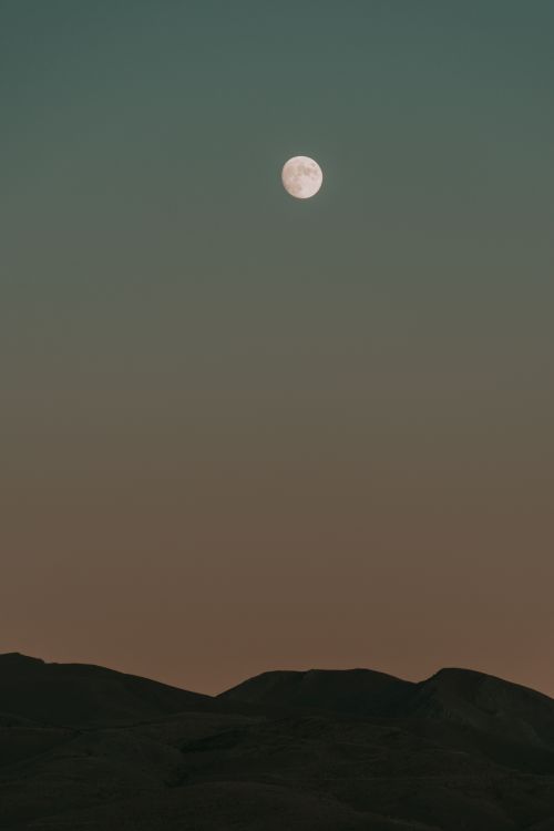 Free A tranquil night scene featuring a full moon illuminating mountains under a clear night sky. Stock Photo