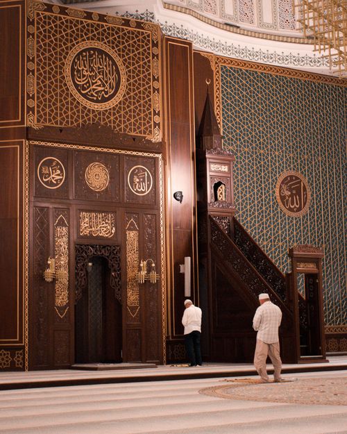 Free Intricately designed mosque interior with two men praying, showcasing Islamic architecture. Stock Photo