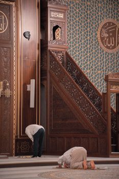 Two men engaged in prayer within a beautifully ornate mosque interior, showcasing intricate Islamic art and design.