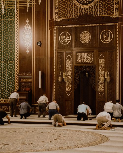 Free Men kneeling in prayer inside a beautifully decorated mosque with intricate Islamic patterns. Stock Photo