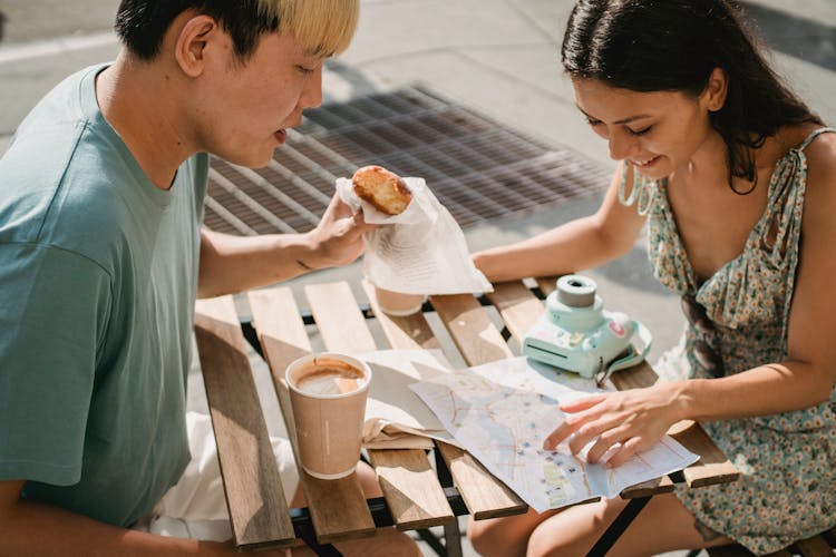 Diverse Couple Having Breakfast In Cafe While Exploring Map