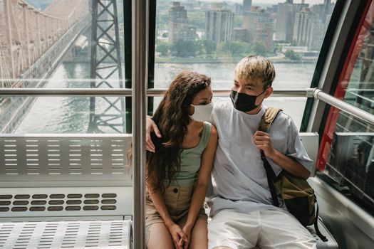 Diverse couple in protective masks in funicular on ropeway