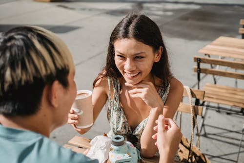 Free From above of positive ethnic girlfriend smiling happily while drinking coffee with boyfriend in outdoor cafe Stock Photo