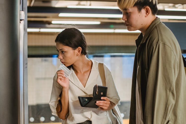 Focused Asian Couple Buying Ticket On Station