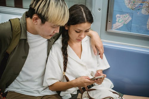 Free Concentrated Asian couple in casual wear sitting in underground subway train and hugging while surfing cellphone during ride home in carriage Stock Photo