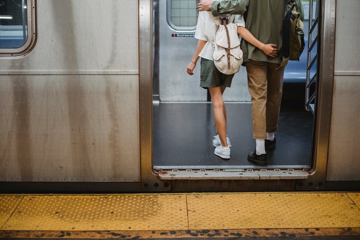 Back view of crop anonymous young couple in stylish outfits hugging while entering wagon of subway train
